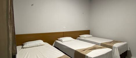 A room with four single beds aligned against a wall, each with a wooden headboard and white bedding.