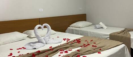 Ein Hotelzimmer mit zwei Betten, eines mit einer Schwanentowel und Rosenblüten, das andere mit einer beigefarbenen Decke.