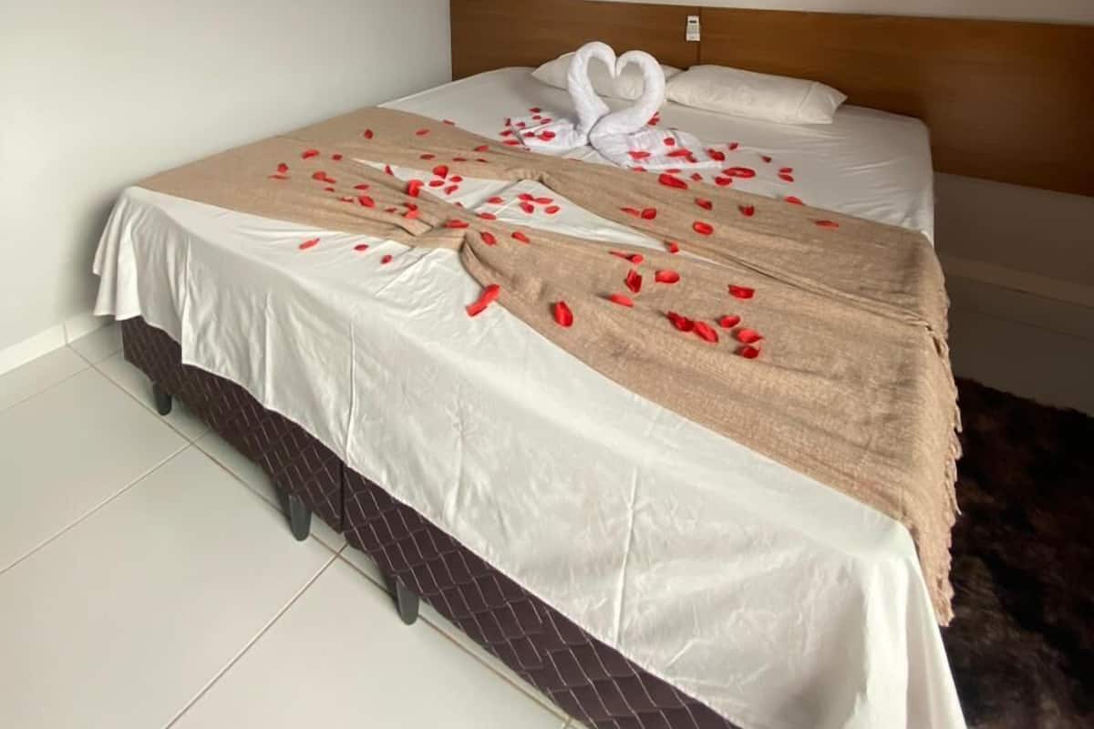 Een netjes opgemaakt bed met rozenblaadjes en een handdoek in de vorm van een hart, een houten hoofdbord en een betegelde vloer.