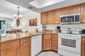 A kitchen with wooden cabinets, a stainless steel microwave, a white dishwasher, and a stove.
