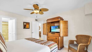 Une chambre d’hôtel avec un lit, une télévision, un fauteuil en osier et un ventilateur de plafond.