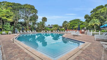 A rectangular swimming pool with a tiled deck surrounding it, equipped with lounge chairs and umbrellas.
