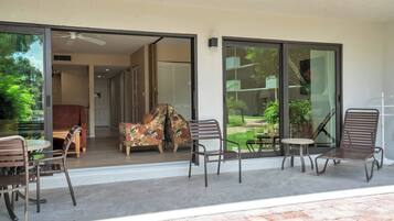 A modern outdoor patio with a glass door leading to a living area, furnished with a sofa, chairs, and a small table.