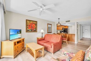 Sala de estar con televisor, sofá, mesa y ventilador de techo.