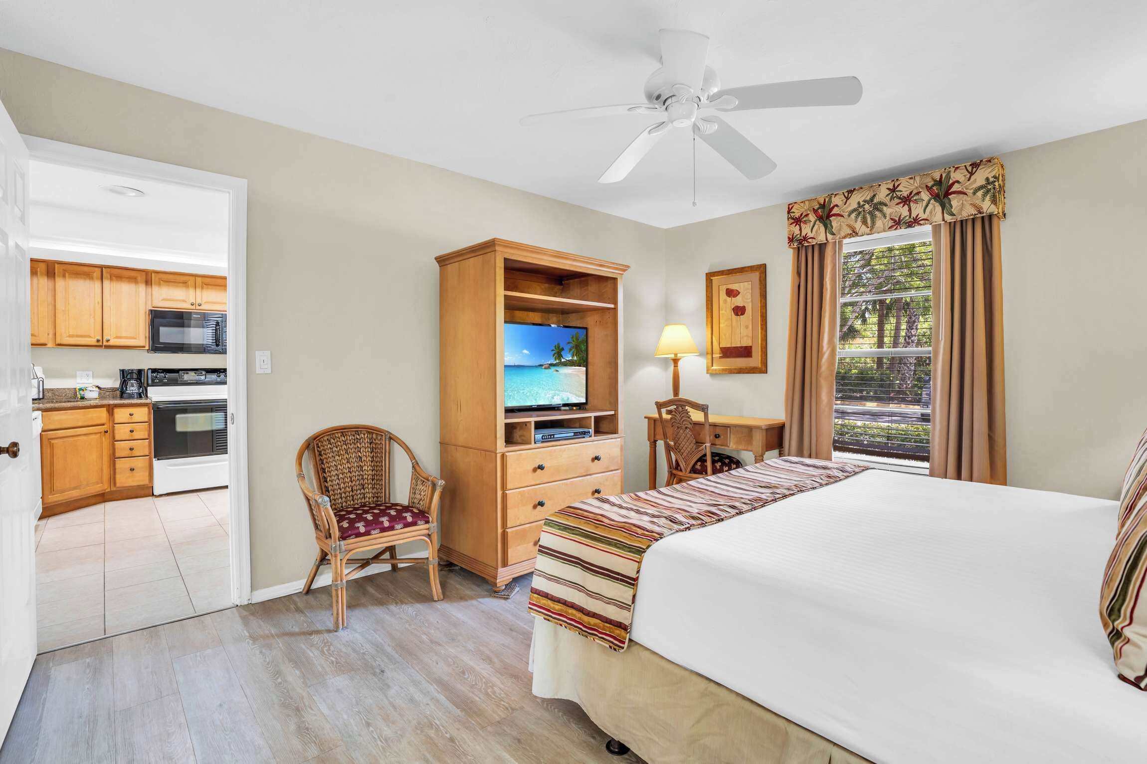 Ein Hotelzimmer mit Bett, Schreibtisch, Stuhl, Kleiderschrank, Deckenventilator und Blick ins Freie.