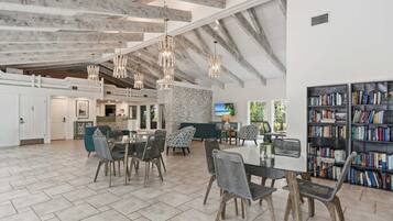 A spacious living area with a high ceiling, exposed beams, and a large bookshelf.