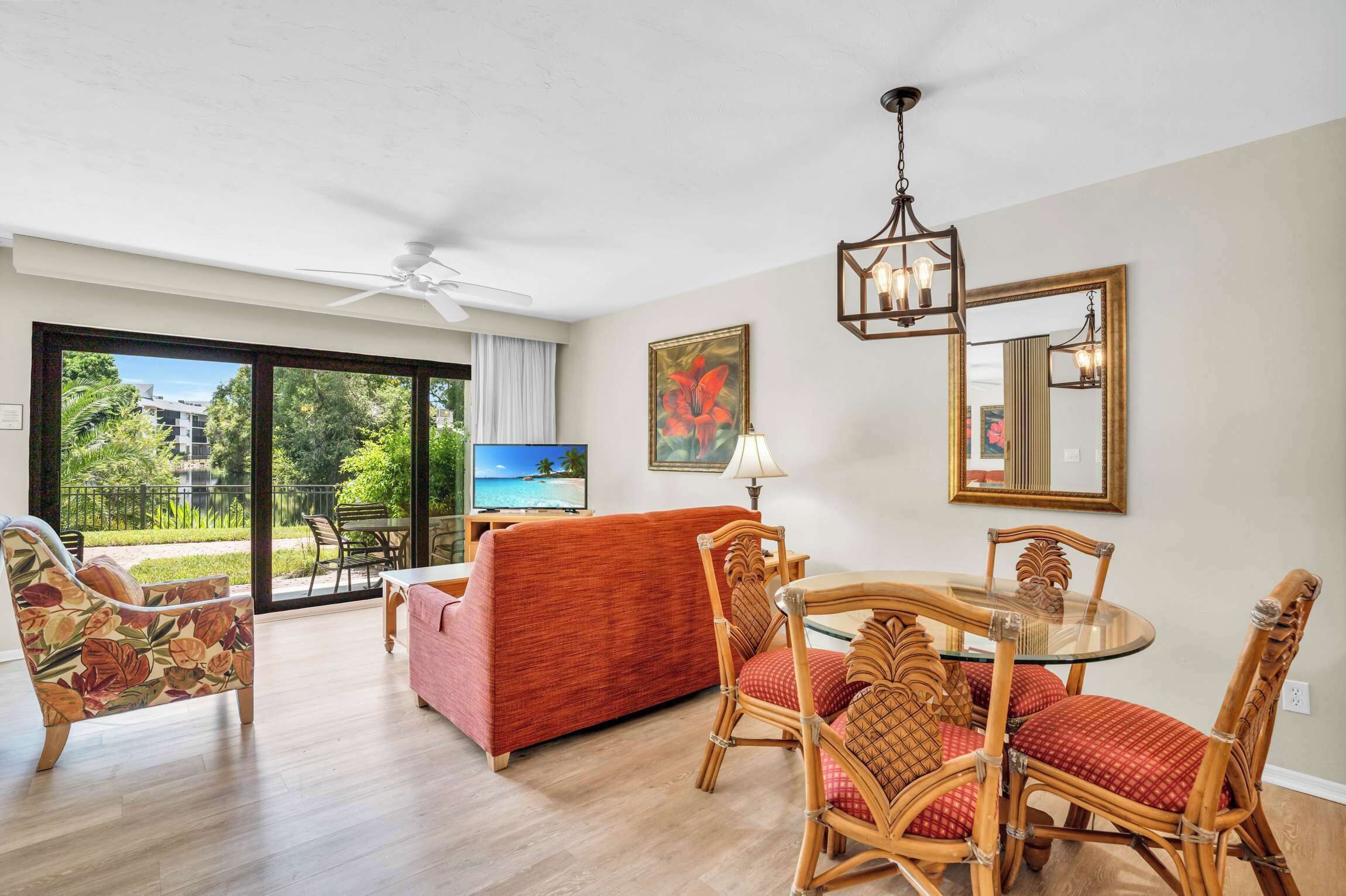 Un salon avec un canapé rouge, des fauteuils en osier, une table en verre, un ventilateur de plafond et un téléviseur.