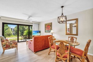 A living room with a red sofa, wicker chairs, a glass table, a ceiling fan, and a TV. - I-151 - First Floor With Resort View & Sleeps 4 (Naples)