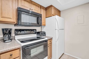 A kitchen with wooden cabinets, a microwave, a stove, a refrigerator, and a coffee maker. - I-450 - Exceptional Lake View 4th Floor Condo! (Naples)