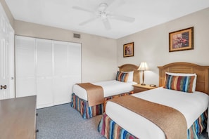 A hotel room with two beds, a ceiling fan, a nightstand with a lamp, and a door with a handle.