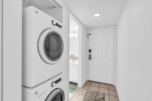 A laundry room with stacked washing machines and a door leading to a bathroom.