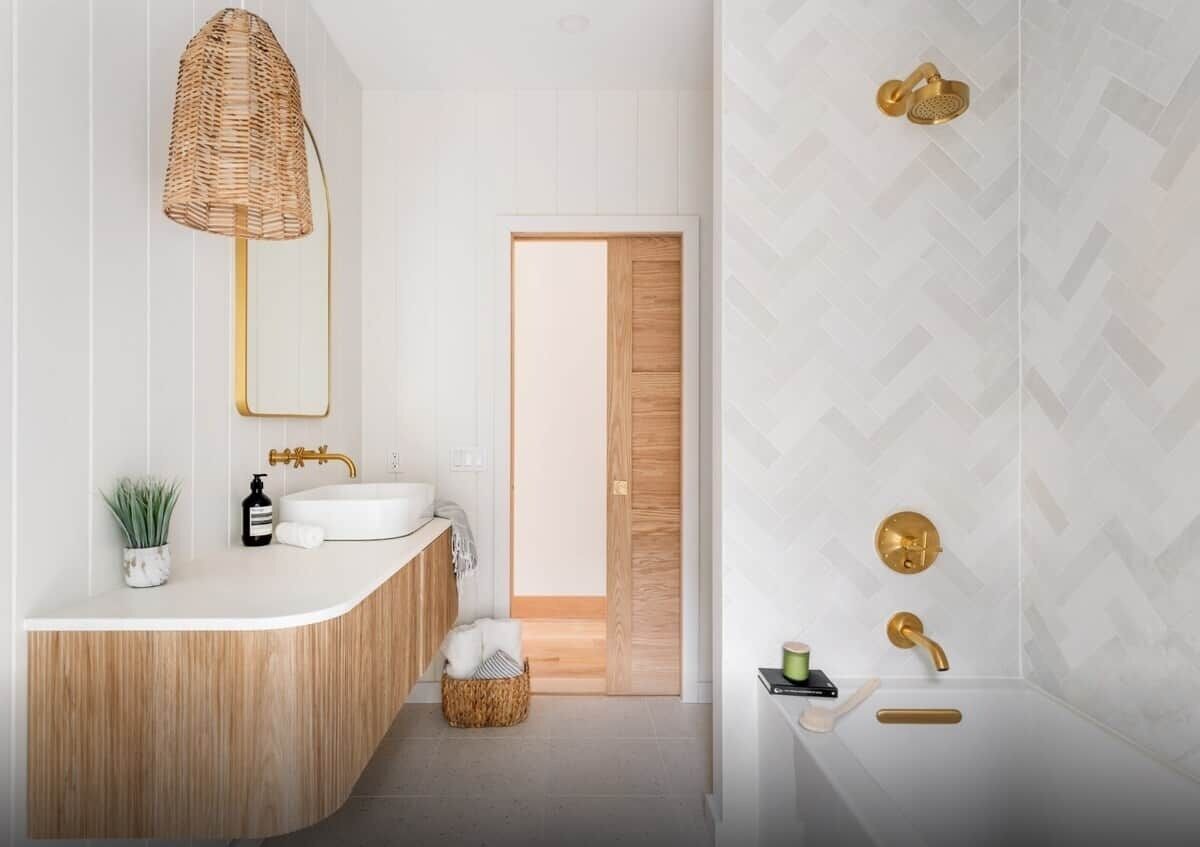A modern bathroom with a wooden vanity, a large mirror, a wicker lamp, and a shower area with gold fixtures.
