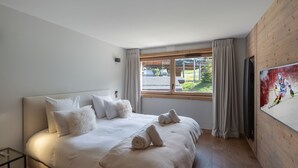 Un dormitorio con una cama grande, un televisor en la pared y una ventana con cortinas.