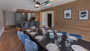 Un comedor moderno con una mesa larga dispuesta para seis comensales, paredes de madera y una cocina al fondo.