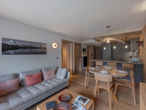 Ein modernes Wohnzimmer mit grauem Sofa, Esstisch aus Holz und einem großen Gemälde an der Wand.