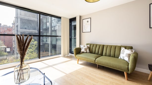 Ein modernes Wohnzimmer mit einem grünen Sofa, einem Glastisch und einer Vase mit getrocknetem Pampasgras.