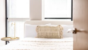 Ein Schlafzimmer mit einem weißen Bett, einem dekorativen Kissen, einer runden Goldlampe und einem weißen Teppich.