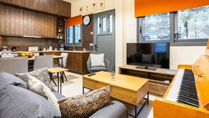 A modern living room with a sofa, coffee table, and a piano. There is a television and a dining area with a kitchen in the background.
