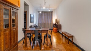 A dining area with a wooden table, black chairs, a bench, a cabinet with glass doors, a sofa, and a curtain.