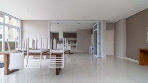 Un'ampia camera moderna con una grande finestra, un tavolo da pranzo in legno e una zona cucina visibile attraverso una porta aperta.