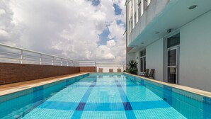 Una piscina sul tetto con piastrelle blu cristalline, una ringhiera bianca e vista sul cielo.