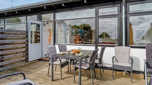 Un área de comedor al aire libre con mesa y sillas, ventanas grandes y una terraza de madera.