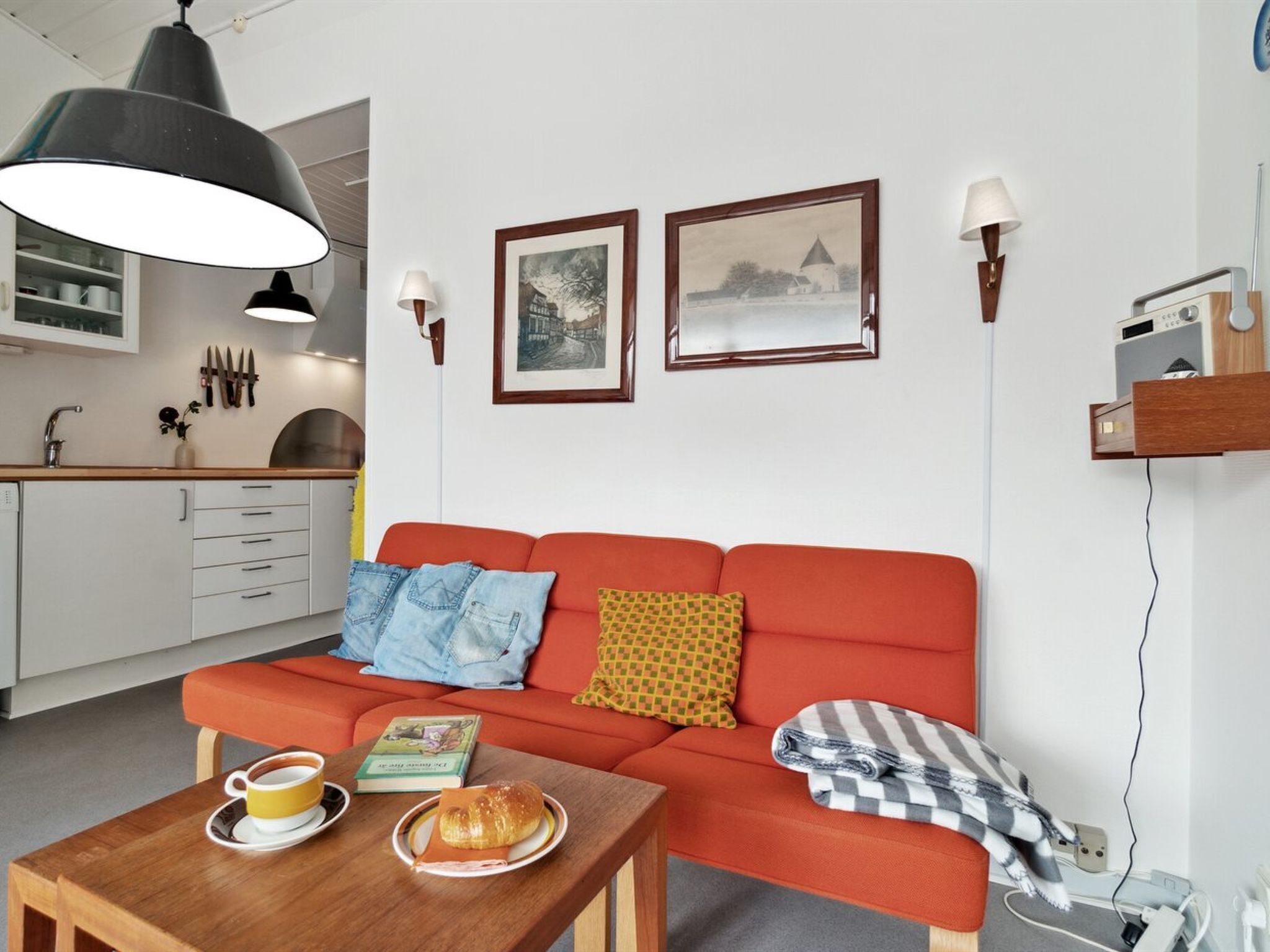 Ein modernes Wohnzimmer mit einem roten Sofa, einem Holztisch und einer Küche im Hintergrund.