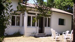 A single-story building with a tiled roof, a covered porch with white chairs, and a small garden area. - Maison D'été Plage a Pied Oleron (Saint-Pierre-d'Oléron)