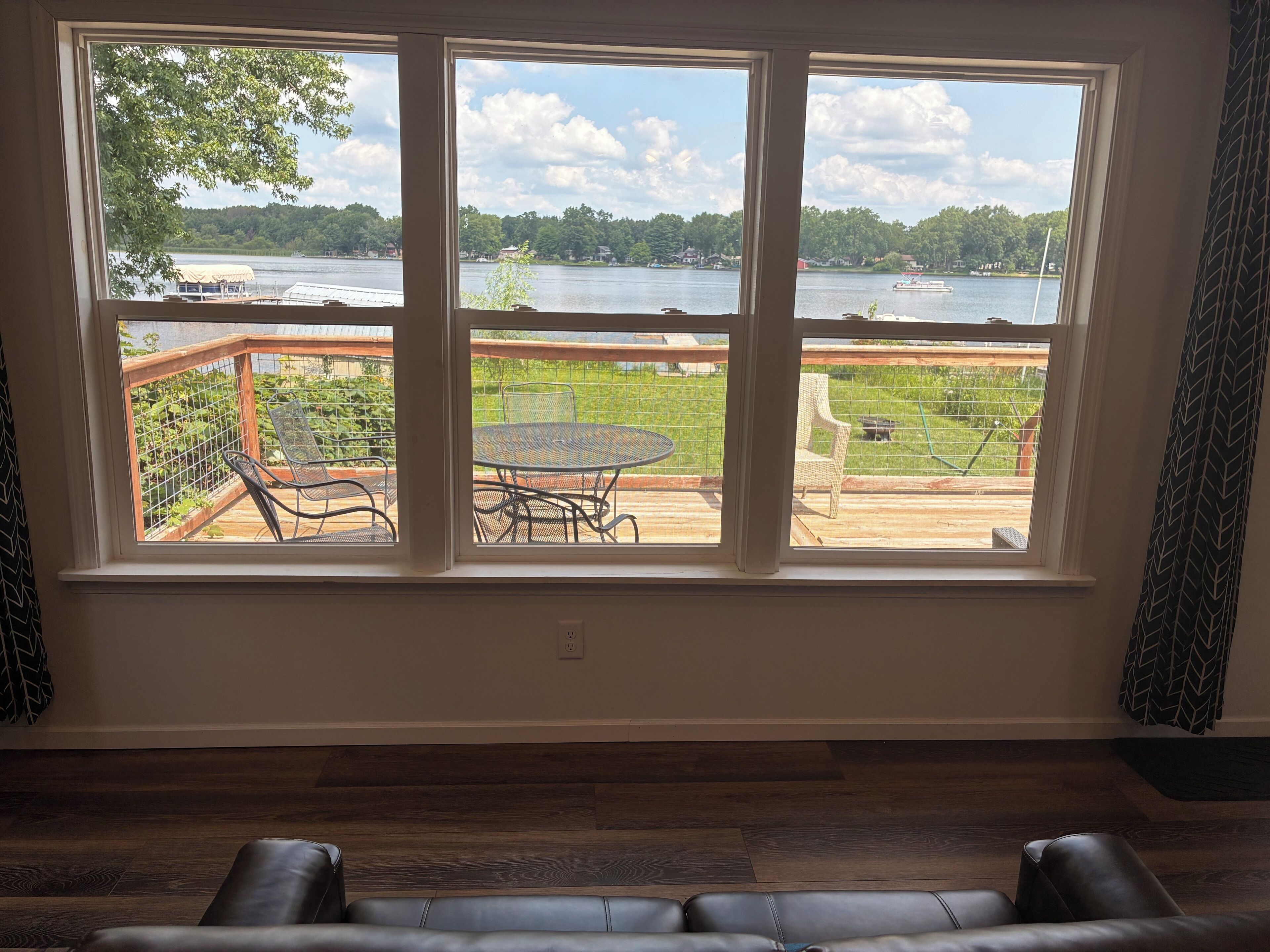 Una habitación con un ventanal grande que da a una terraza con muebles de exterior y vistas a un lago.