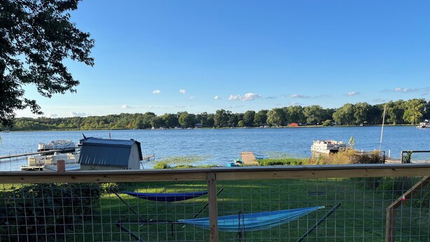 Una terraza de madera con una hamaca y un kayak, con vistas a un lago con botes y un muelle.