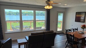 A room with a large window overlooking a lake, a ceiling fan, a wooden dining table with chairs, and a sofa. - Relax and Unwind at the Cozy Cabin on Heaton Lake. (Elkhart)