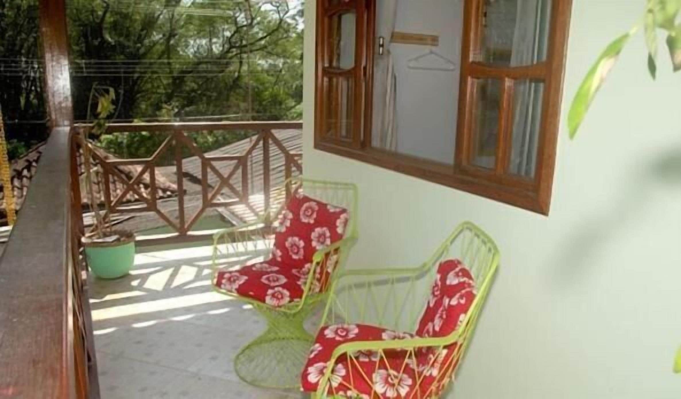 A balcony with two green chairs with red floral cushions, a wooden railing, and a view of trees.