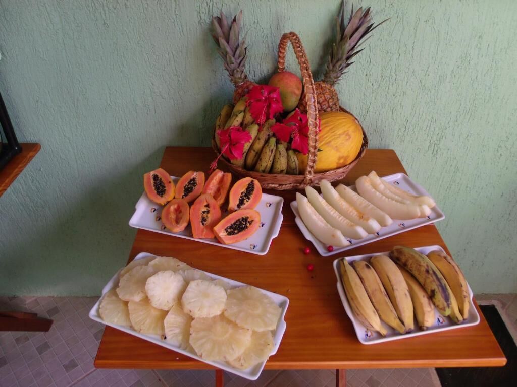 A table with various fruits and a basket of pineapples and mangoes.