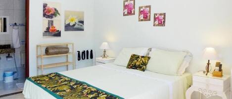 A hotel room with a bed, bedside tables, a wooden shelf, and artwork on the walls.