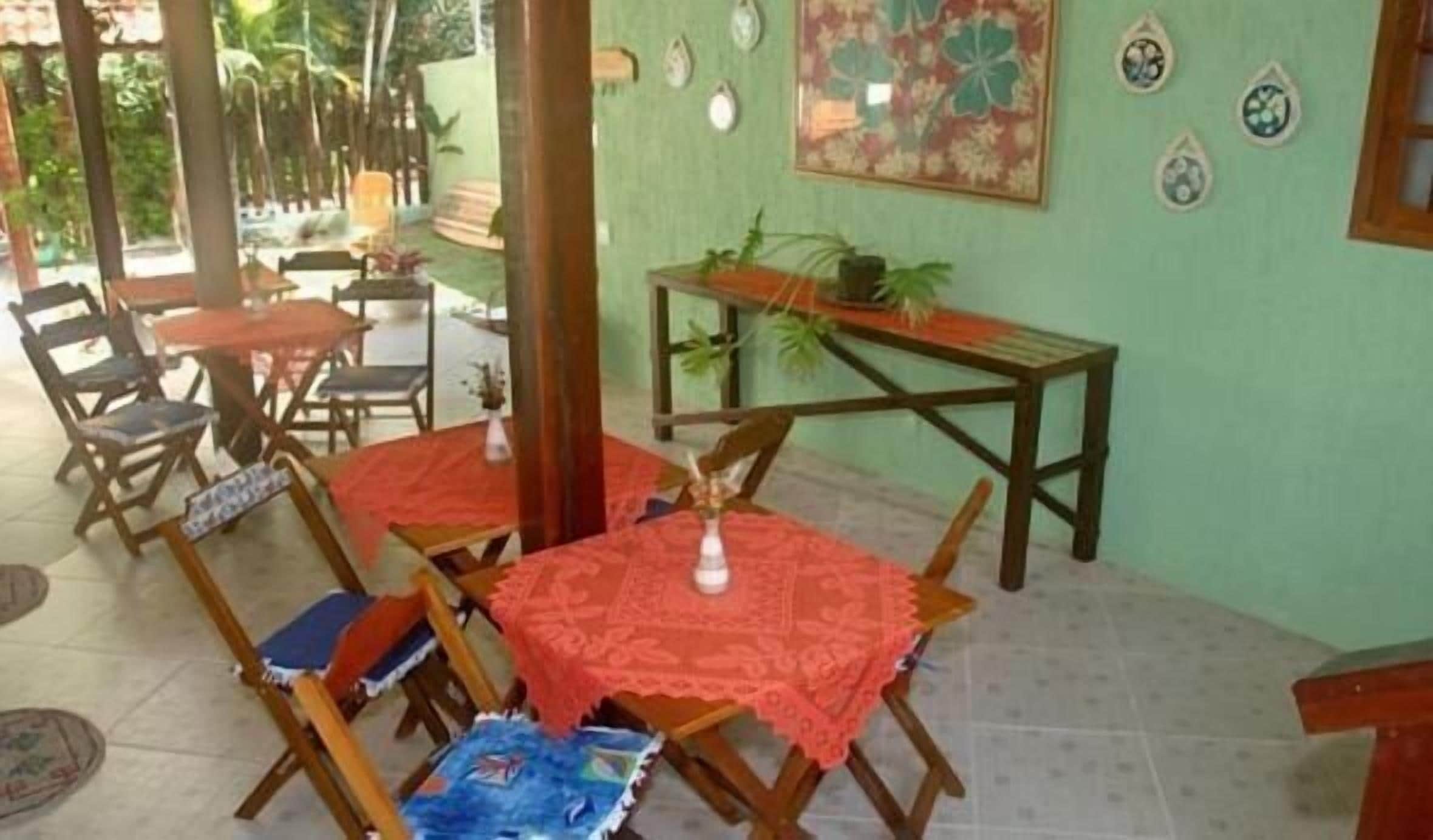A covered patio area with wooden tables and chairs, a small table with a plant, and decorative plates on the wall.