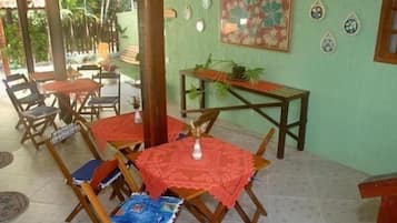 A covered patio area with wooden tables and chairs, a small table with a plant, and decorative plates on the wall.