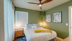 A bedroom with a bed, bedside table, lamp, ceiling fan, and artwork on the wall.