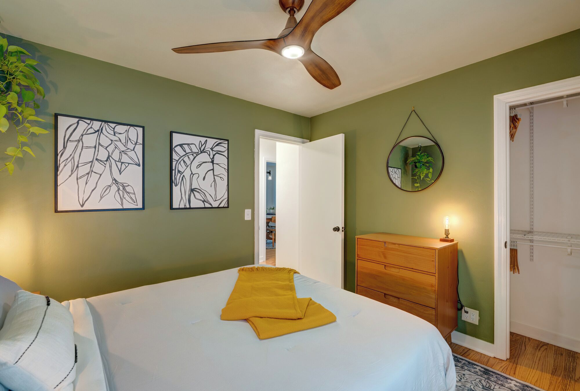 A bedroom with a bed, a ceiling fan, a wooden dresser, and two wall art pieces.