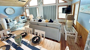 A spacious living area with a high ceiling, a dining table set for four, and a comfortable seating arrangement. - Oceanside home in Corolla with 4 bedrooms, 3 baths and private pool. (Corolla)