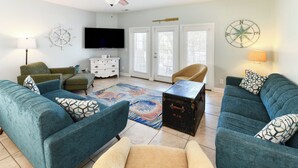 A living room with teal sofas, a wooden coffee table, a television, and decorative items like a compass and a ship's wheel. - Walk to the Beach 5 BR Beach House with a Private Pool! I Choose You  (Surfside Beach)