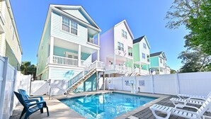 A swimming pool with lounge chairs, a staircase leading to a balcony, and colorful houses in the background. - Walk to the Beach 5 BR Beach House with a Private Pool! I Choose You  (Surfside Beach)