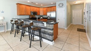 A kitchen with wooden cabinets, a stainless steel refrigerator, a microwave, and a built-in island with bar stools. - Walk to the Beach 5 BR Beach House with a Private Pool! I Choose You  (Surfside Beach)
