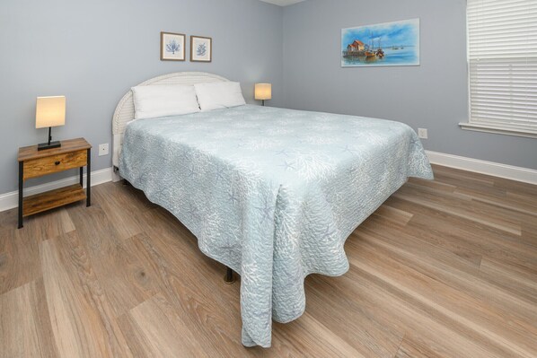 A bedroom with a bed, nightstands, a painting, and a window with blinds.