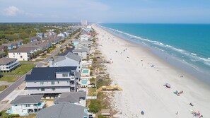 An aerial view of a coastal residential area with houses, a beach, and a clear sky.