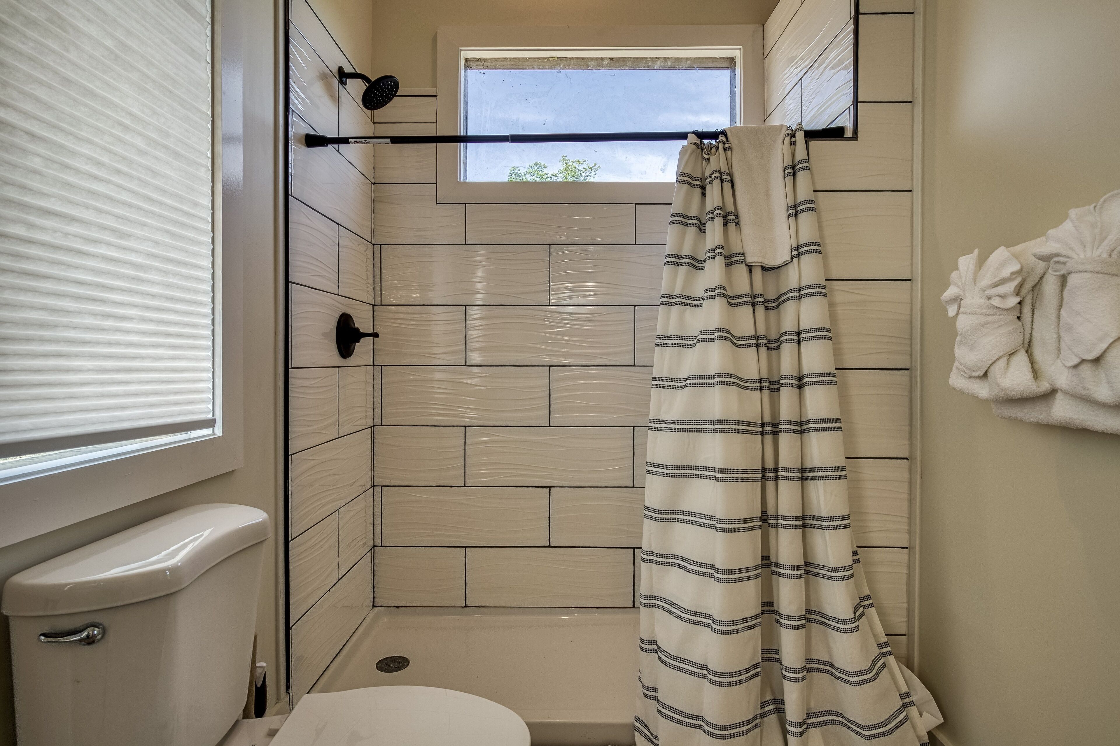 Une petite salle de bain avec un rideau de douche, des toilettes et une fenêtre.