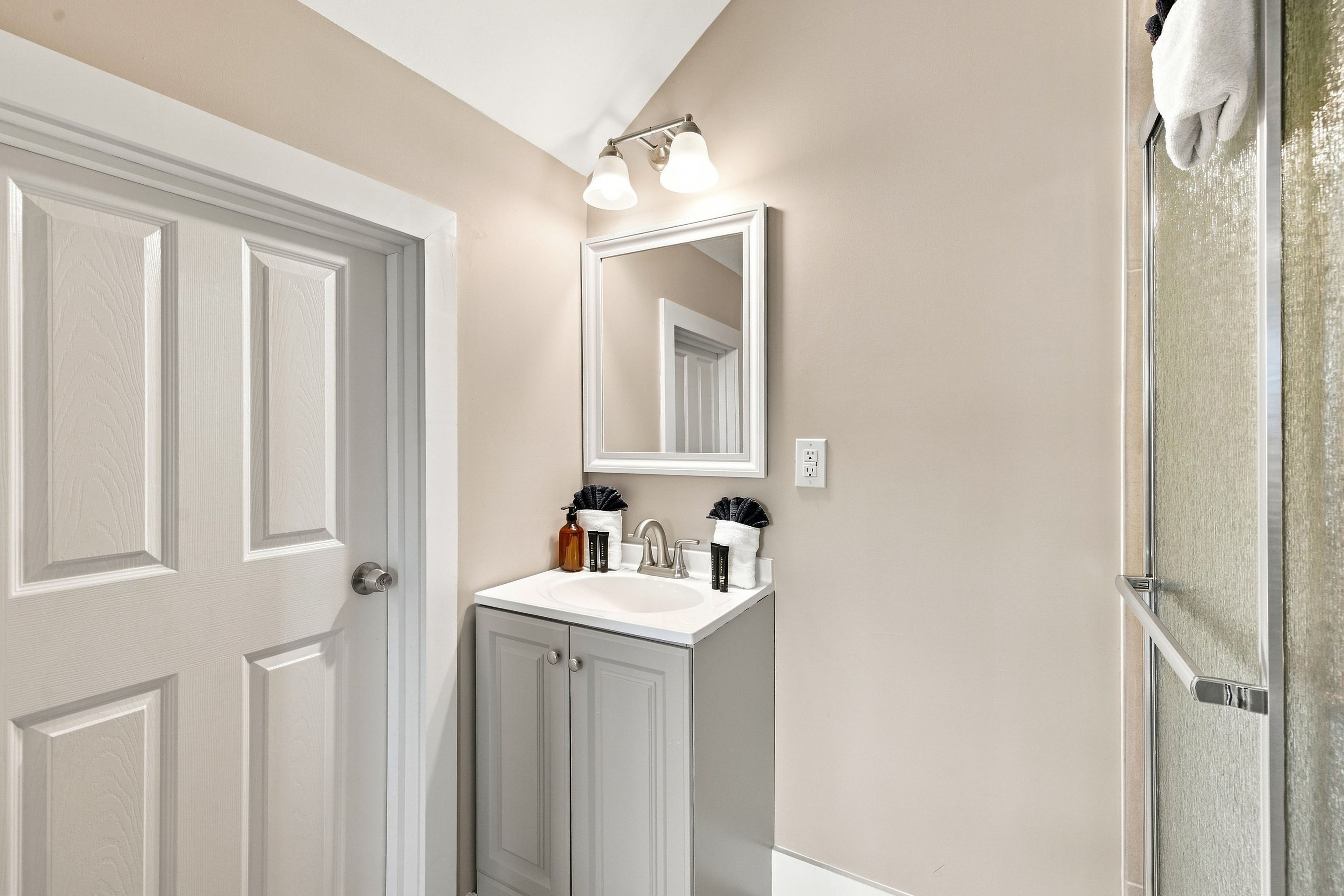 Un bagno con una porta bianca, un lavabo con uno specchio sopra e un asciugamano appeso al muro.