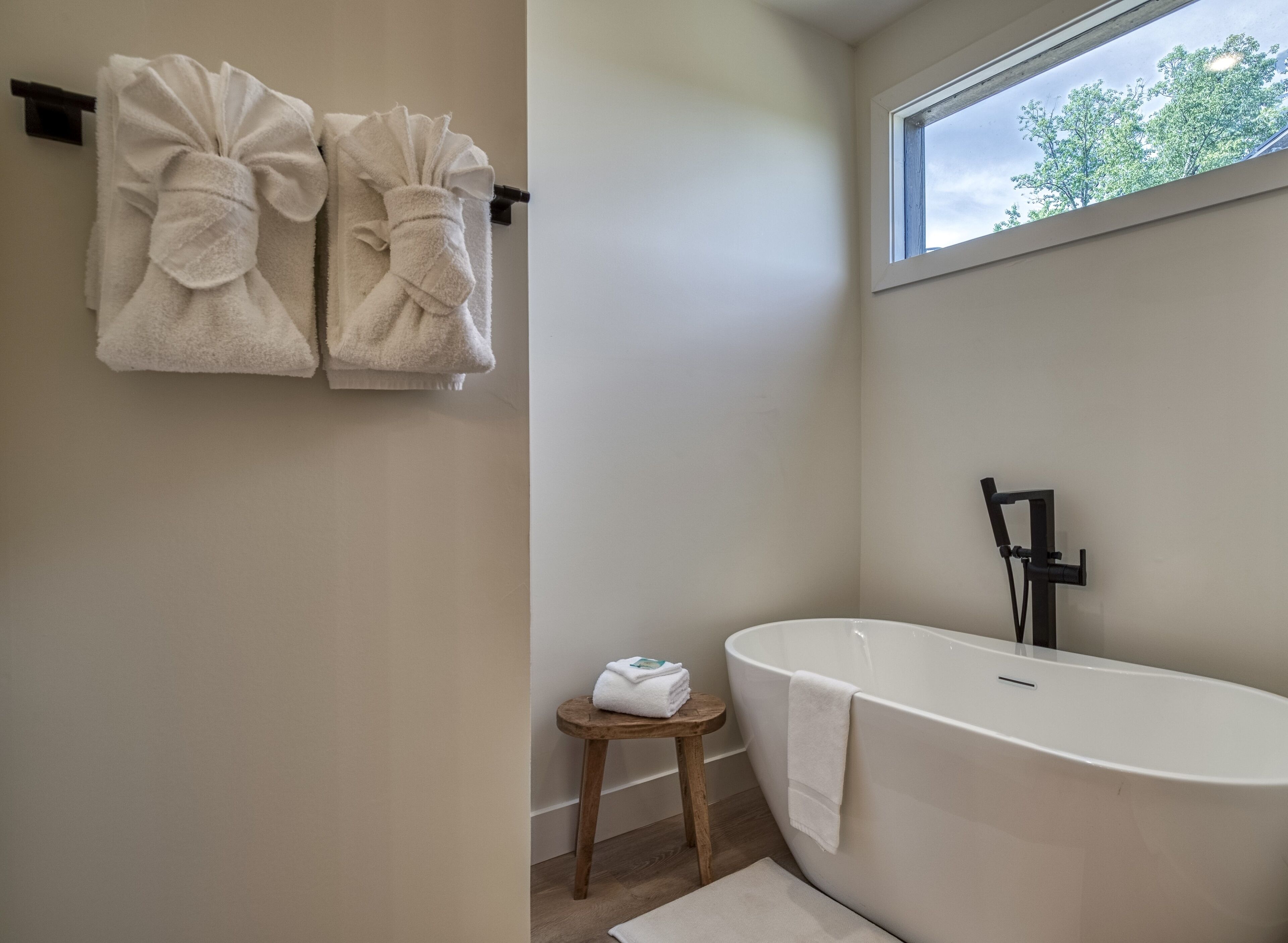 A modern bathroom with a freestanding bathtub, a wooden stool, and two towels on a towel rack.