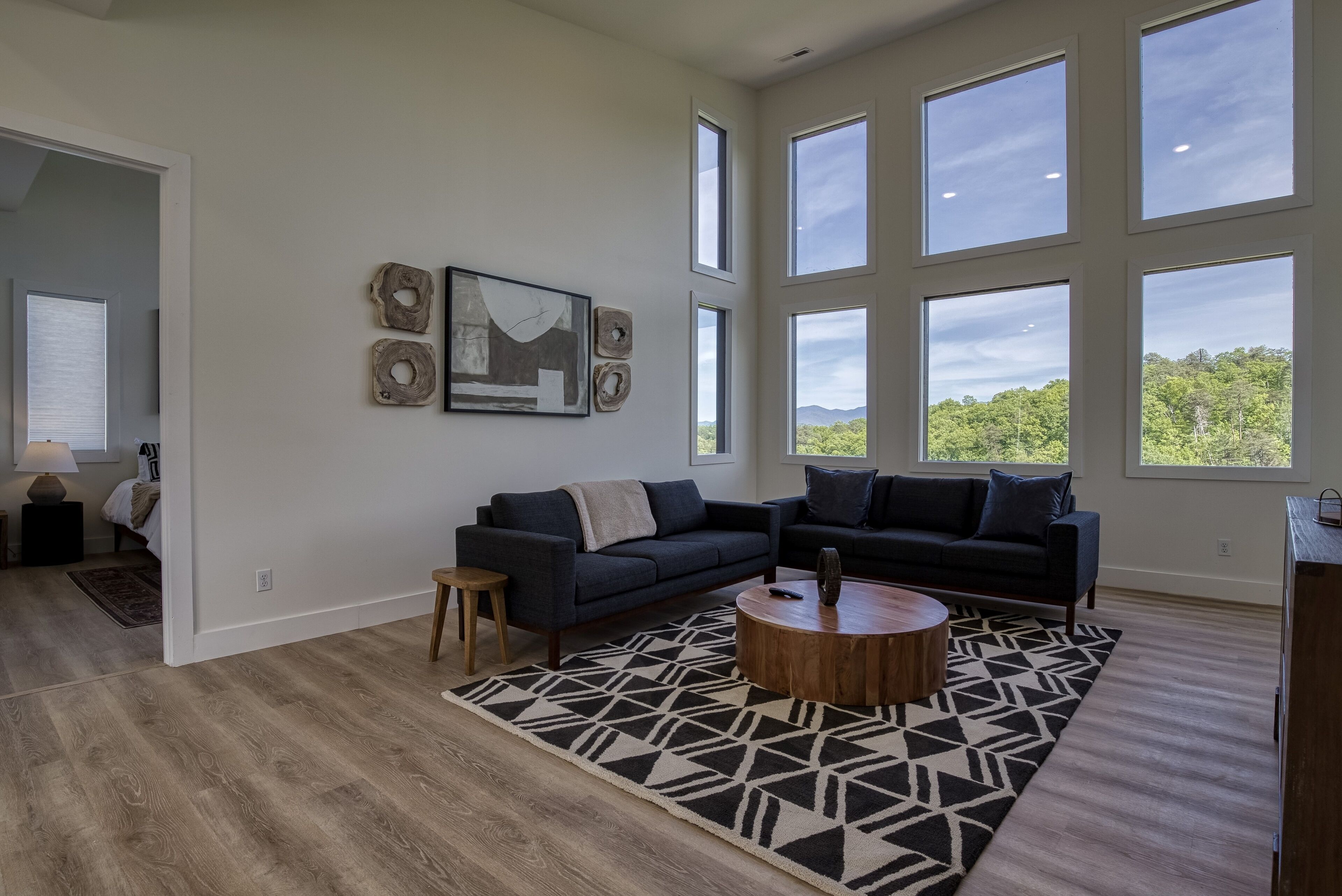 A spacious living room with a large window, a dark-colored sofa, a wooden coffee table, and a patterned rug.