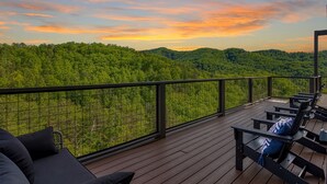 A wooden deck with outdoor seating and a view of a forested landscape. - Panoramic Paradise 4 Bedroom Cabin by RedAwning (Sevierville)