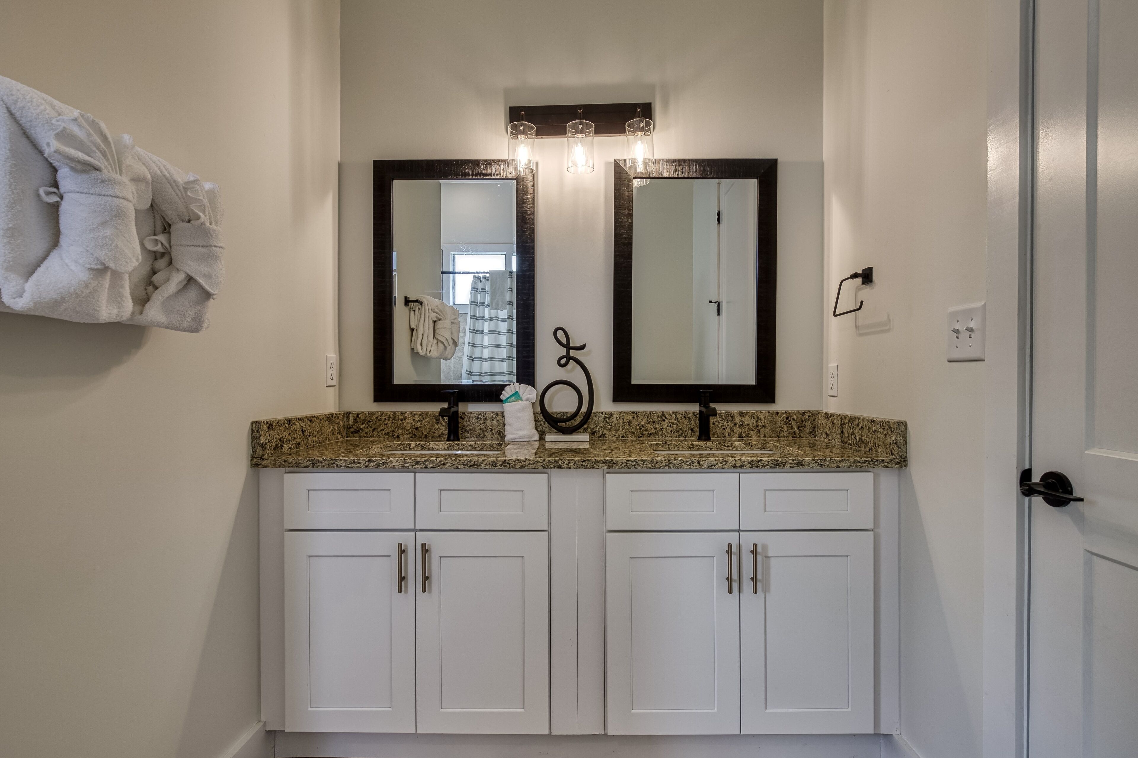 A bathroom with a double vanity, white cabinets, and a granite countertop.